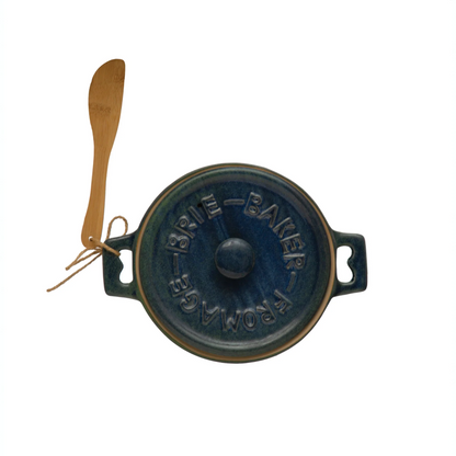 Top view of a reactive glazed blue and green lidded stoneware baking dish with a wooden spoon tied to one handle with twine against a white background. Lid has the raised words 'BRIE-BAKER-FROMAGE'  