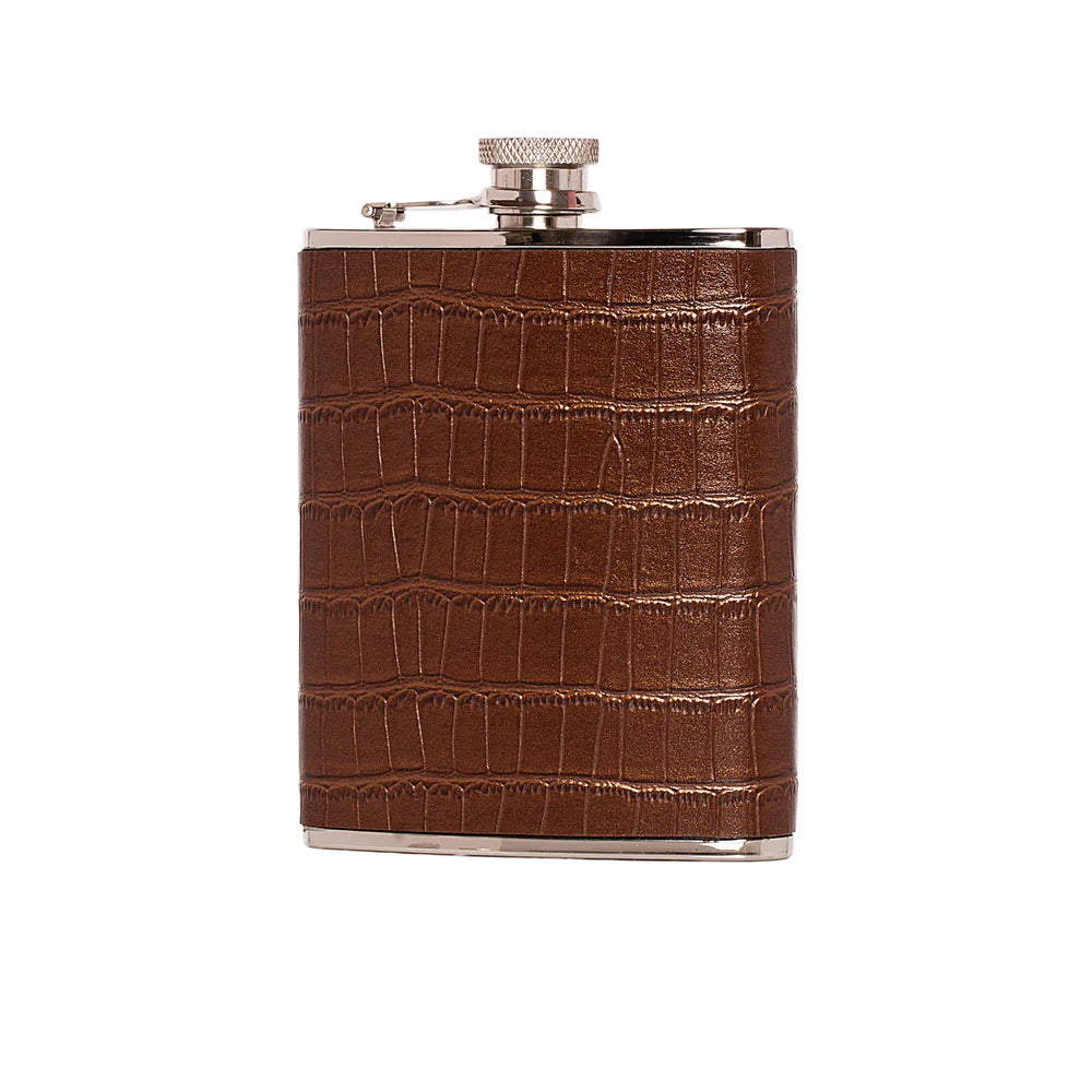 A stainless steel flask wrapped in a brown crocodile-embossed leather sleeve against a white background.