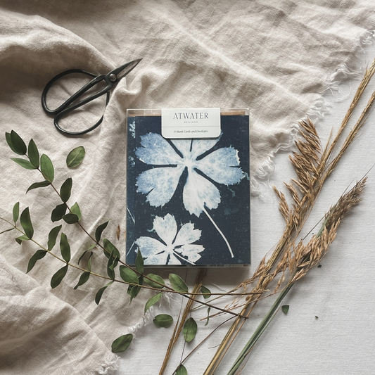Blue and white botanical notecard set packaged in a clear box and surrounded by plants and garden sheers on a linen cloth