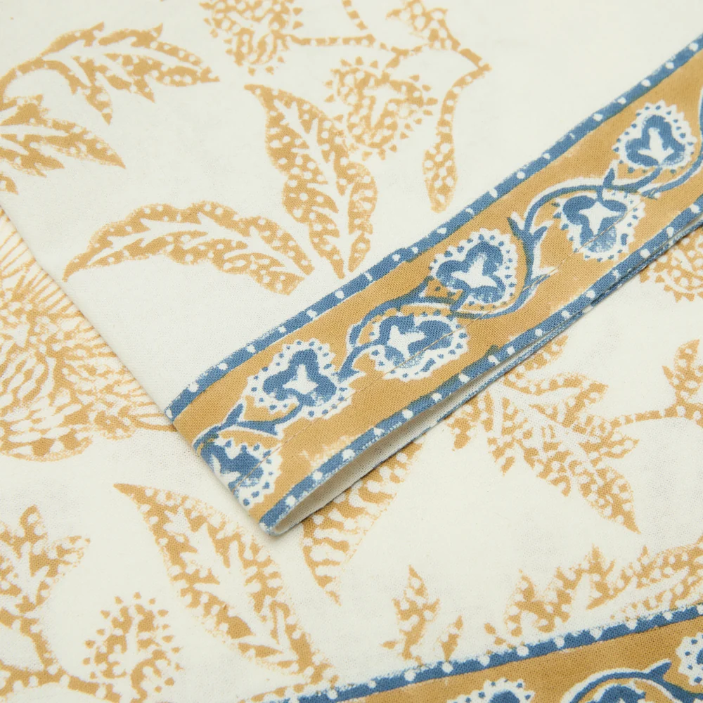 Muted mustard and blue floral printed border detail of a cotton napkin.