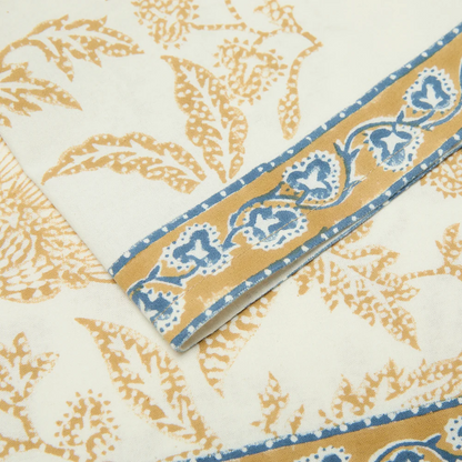 Muted mustard and blue floral printed border detail of a cotton napkin.