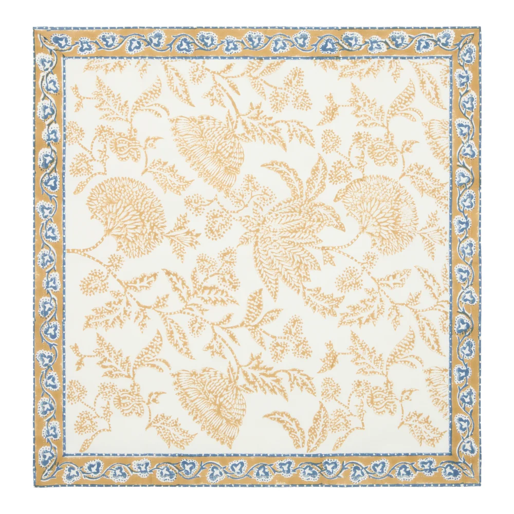 A square cream-colored cotton napkin featuring a block-printed floral pattern in a muted deep mustard and blue shown against a white background.