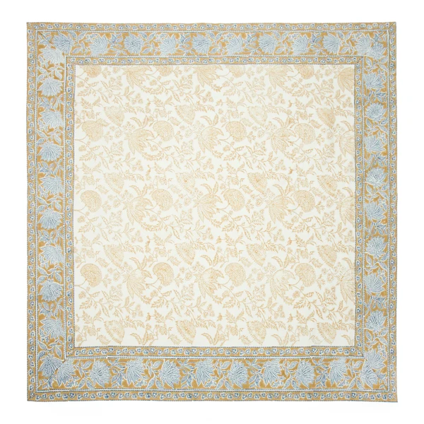 A cream-colored square tablecloth featuring a central block-printed floral pattern in a muted deep mustard yellow framed with a deep mustard border with a repeating blue floral print.