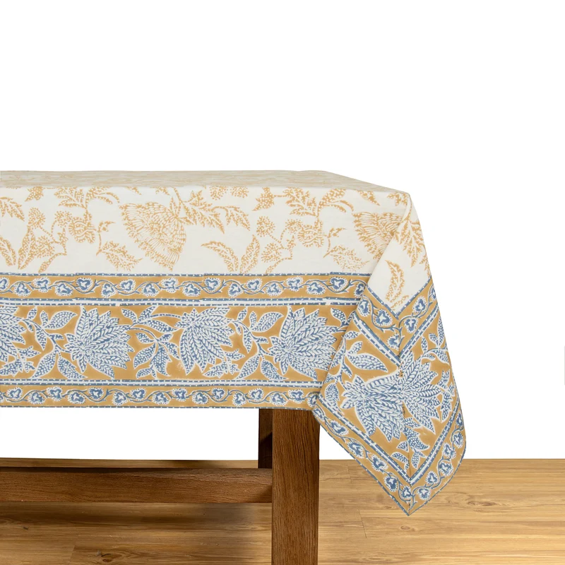A cream-colored tablecloth featuring a block-printed floral pattern in a muted deep mustard and blue draped over a wooden table.