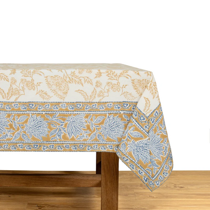 A cream-colored tablecloth featuring a block-printed floral pattern in a muted deep mustard and blue draped over a wooden table.