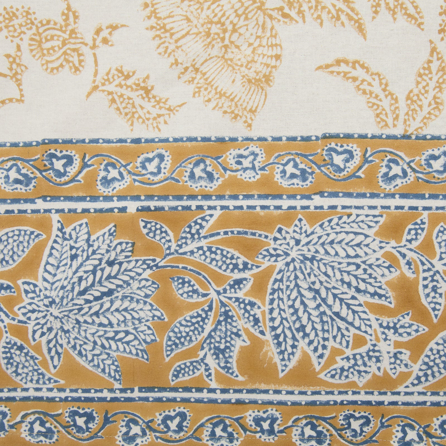 Detail of the deep mustard and blue floral printed border of a cotton tablecloth.