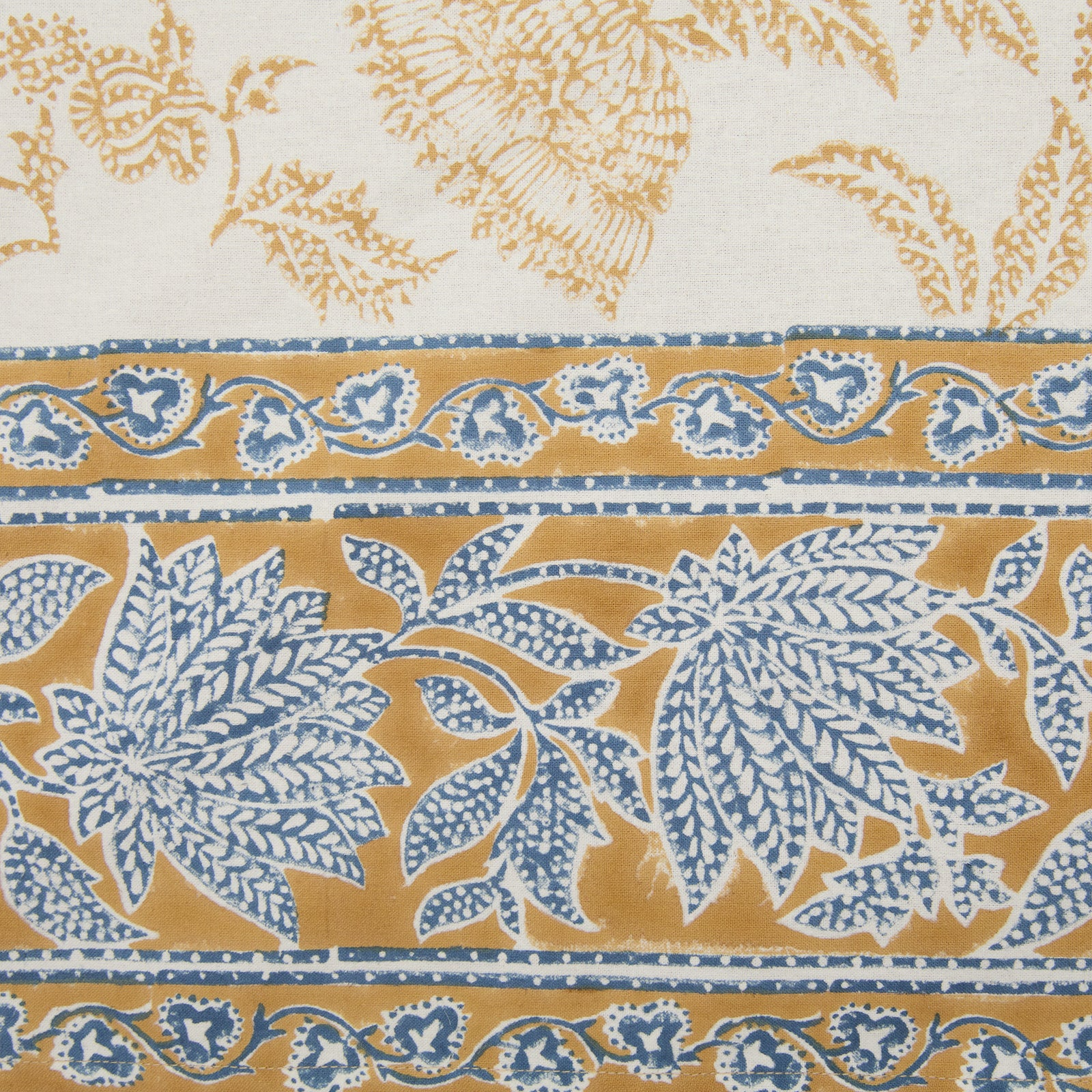 Detail of the deep mustard and blue floral printed border of a cotton tablecloth.
