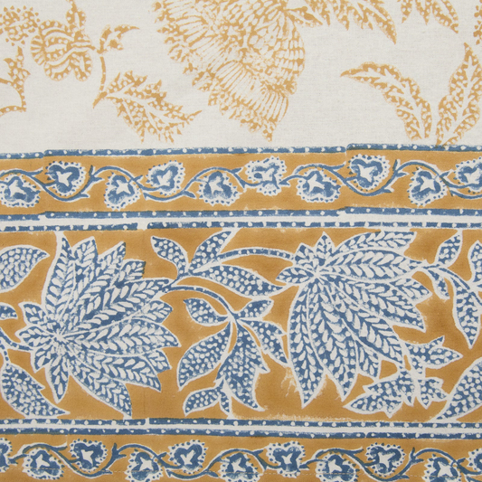 Detail of the deep mustard and blue floral printed border of a cotton tablecloth.