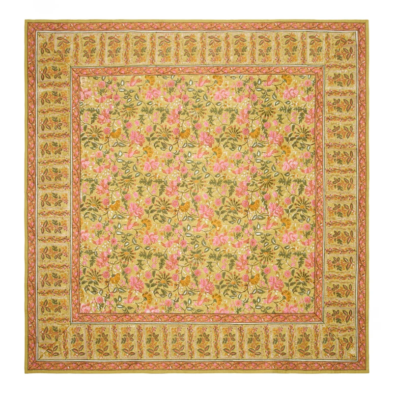 A square mustard-colored tablecloth with a traditional block-printed floral pattern in olive green, saffron, and rose pink, and a contrasting repeated leaf border laid flat against a white background.