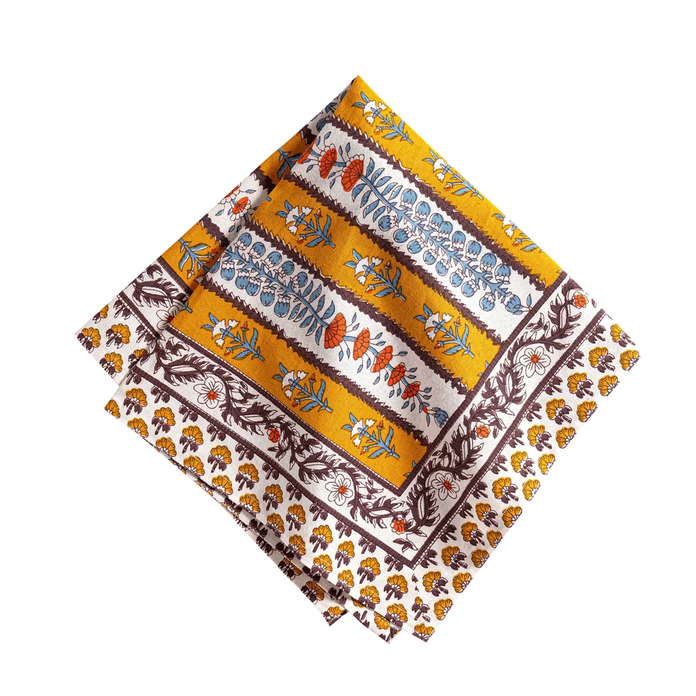 Folded cloth napkin with a mustard yellow, off-white and mahogany brown striped pattern and decorated with block printed light blue and burnt orange floral motifs on a white background