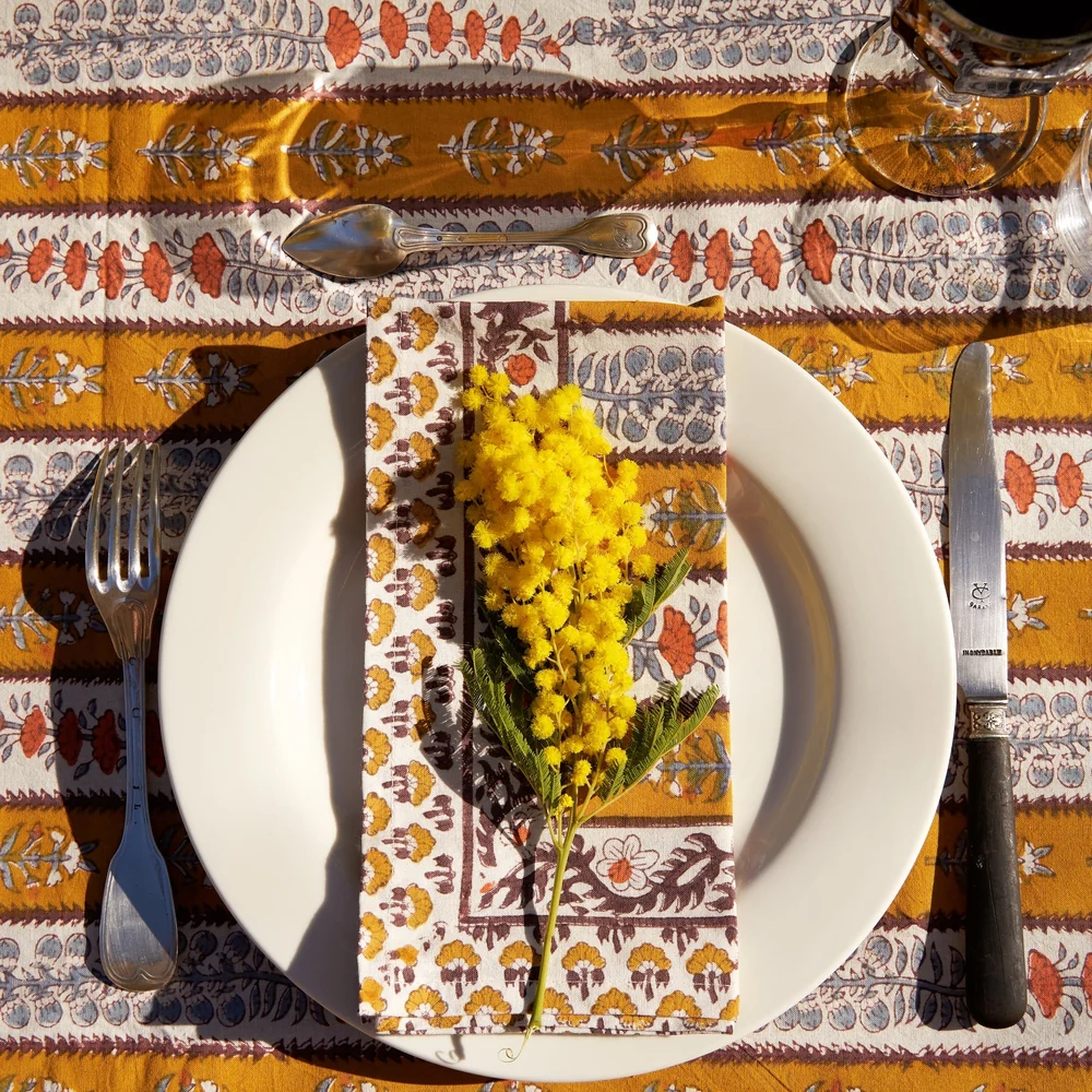 Dining table setting with a striped and floral block printed tablecloth with a matching napkin on a white plate surrounded by drinkware and flatware