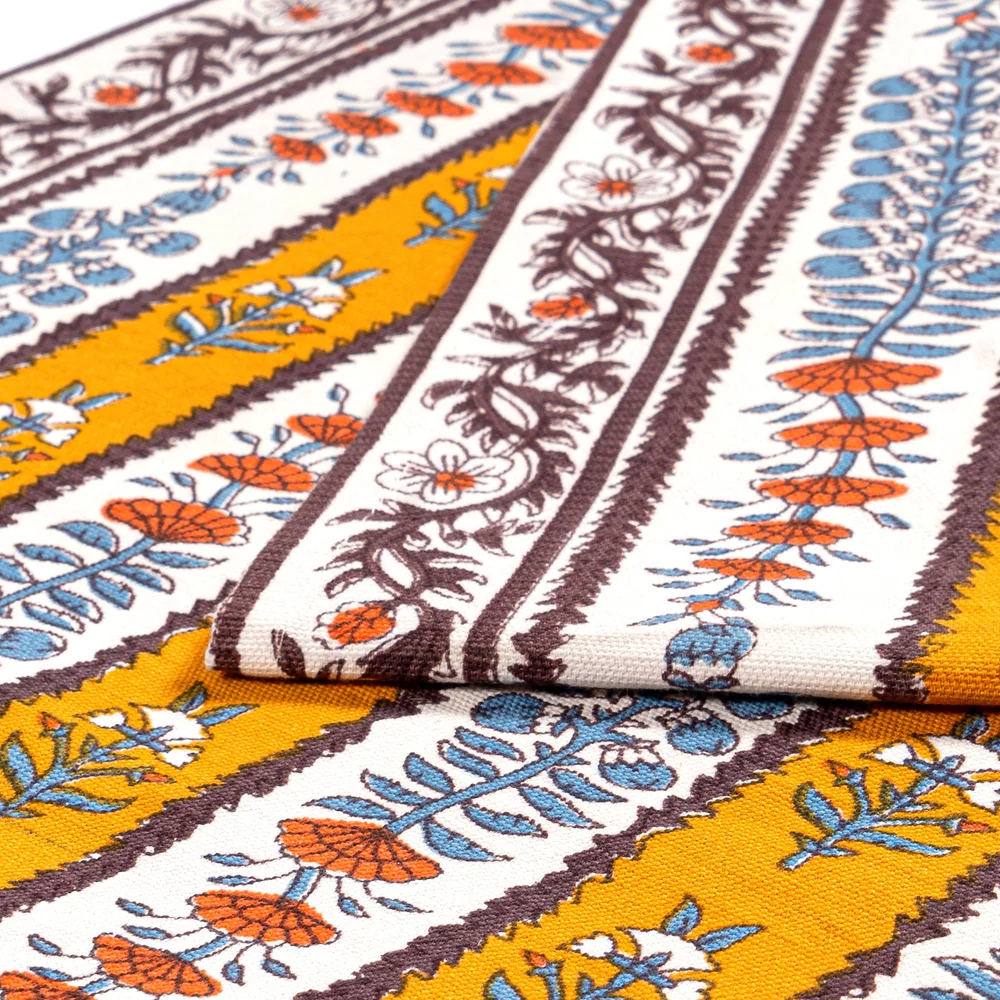 Close-up detail of block printed floral table runner in mustard yellow, off-white, mahogany brown, burnt orange and light blue.