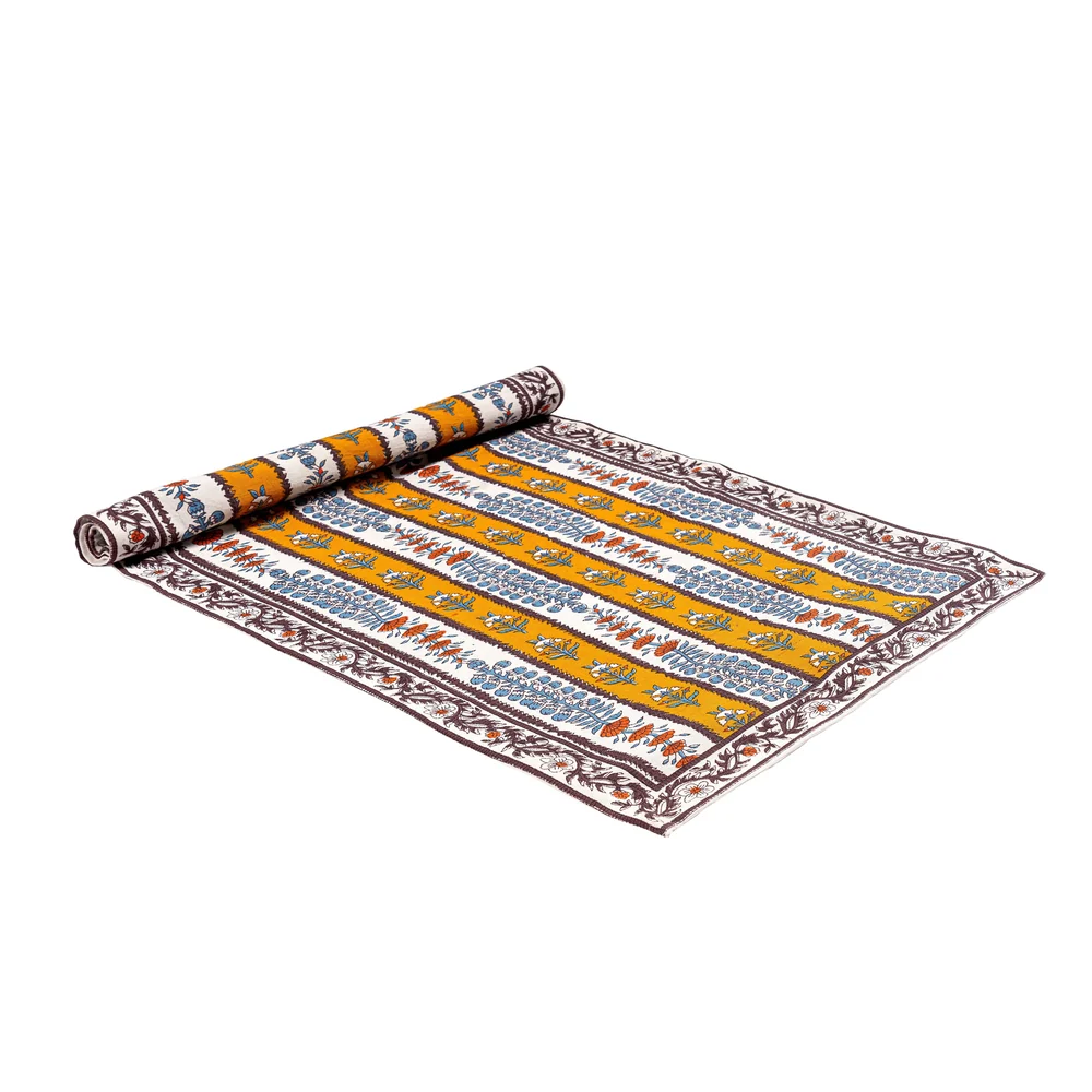 A partially rolled table runner featuring an off-white and mustard yellow striped pattern decorated with mahogany brown, light blue and burnt orange floral block printed motifs against a white background.