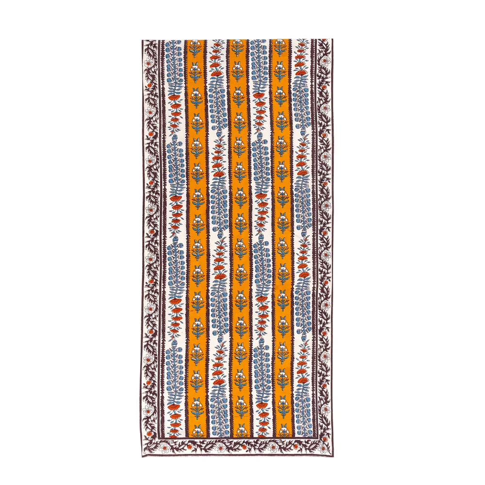 An off-white and mustard yellow striped table runner decorated with block printed mahogany brown, light blue and burnt orange floral motifs against a white background.