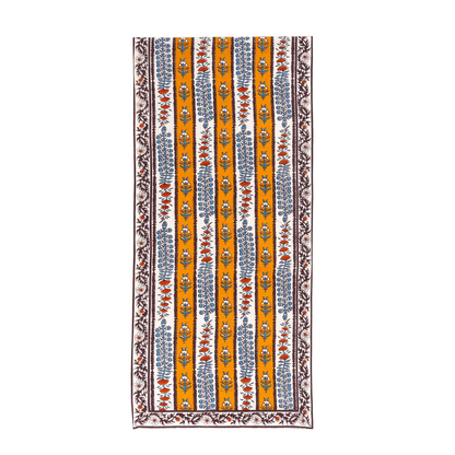 An off-white and mustard yellow striped table runner decorated with block printed mahogany brown, light blue and burnt orange floral motifs against a white background.