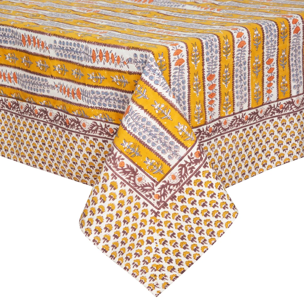 A close-up of a printed tablecloth with repeating yellow, off-white and brown stripes decorated with block-printed floral motifs in light blue and orange.