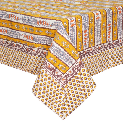 A close-up of a printed tablecloth with repeating yellow, off-white and brown stripes decorated with block-printed floral motifs in light blue and orange.