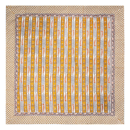 A square block printed tablecloth laid flat on a white background, featuring vertical stripes with intricate floral patterns in mustard yellow, white, light blue and orange-red, surrounded by a wide repeating floral pattern border.