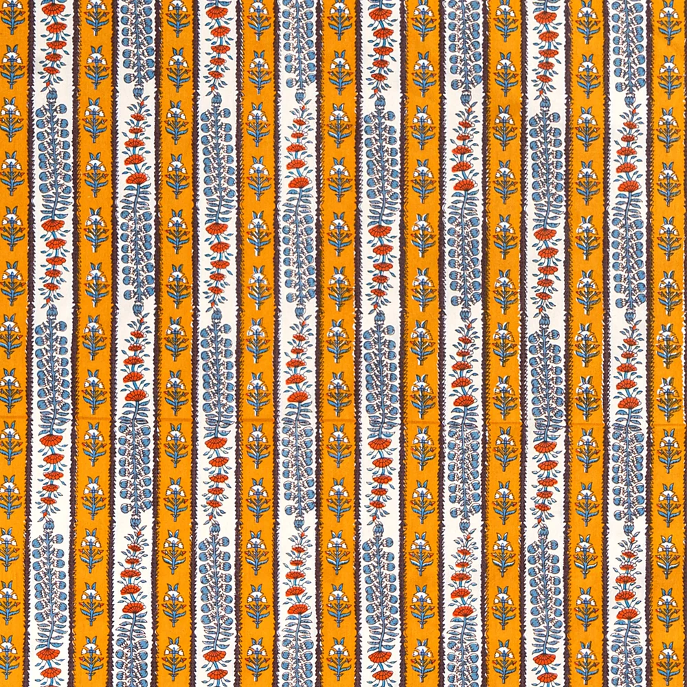 A close-up of a block printed, vertically striped tablecloth featuring alternating bands of mustard yellow and white, separated by dark brown, decorated with blue and rust-orange botanical motifs.