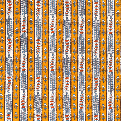 A close-up of a block printed, vertically striped tablecloth featuring alternating bands of mustard yellow and white, separated by dark brown, decorated with blue and rust-orange botanical motifs.