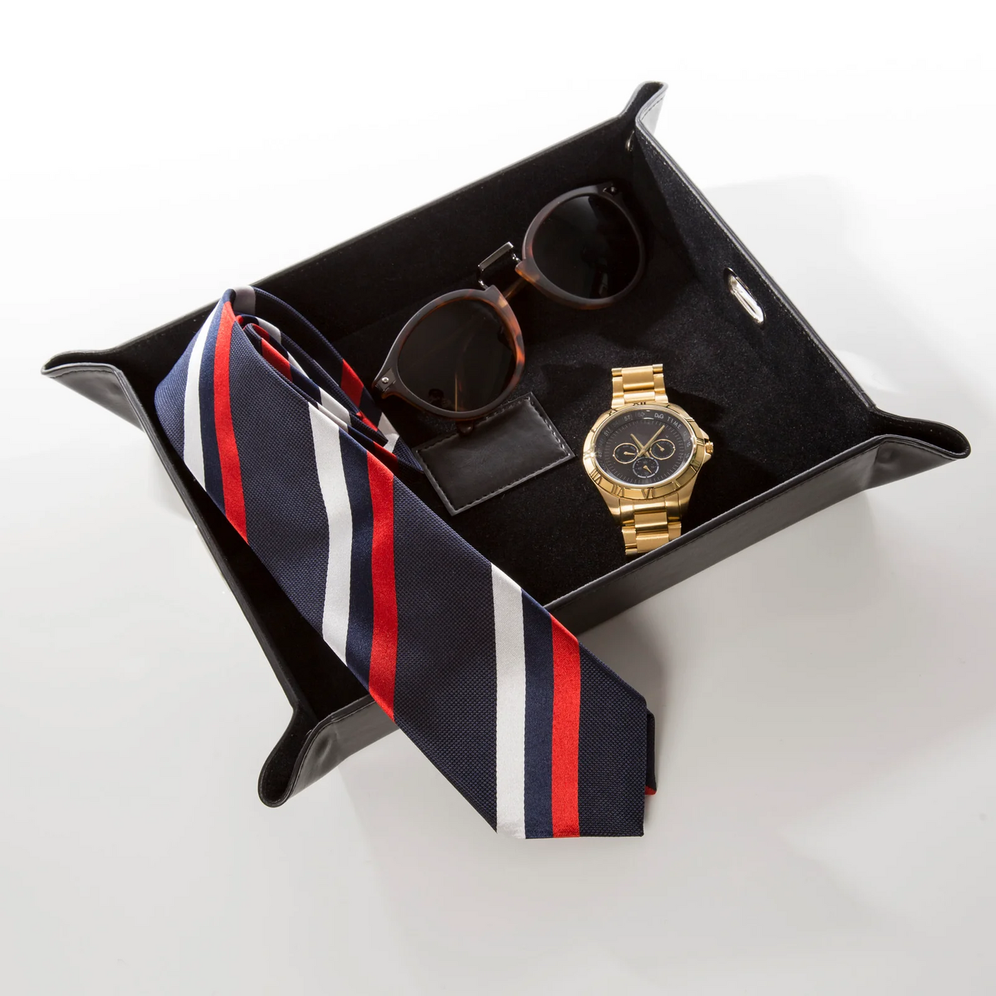 Black leather valet tray holding a striped tie, sunglasses and a wristwatch against a white background.
