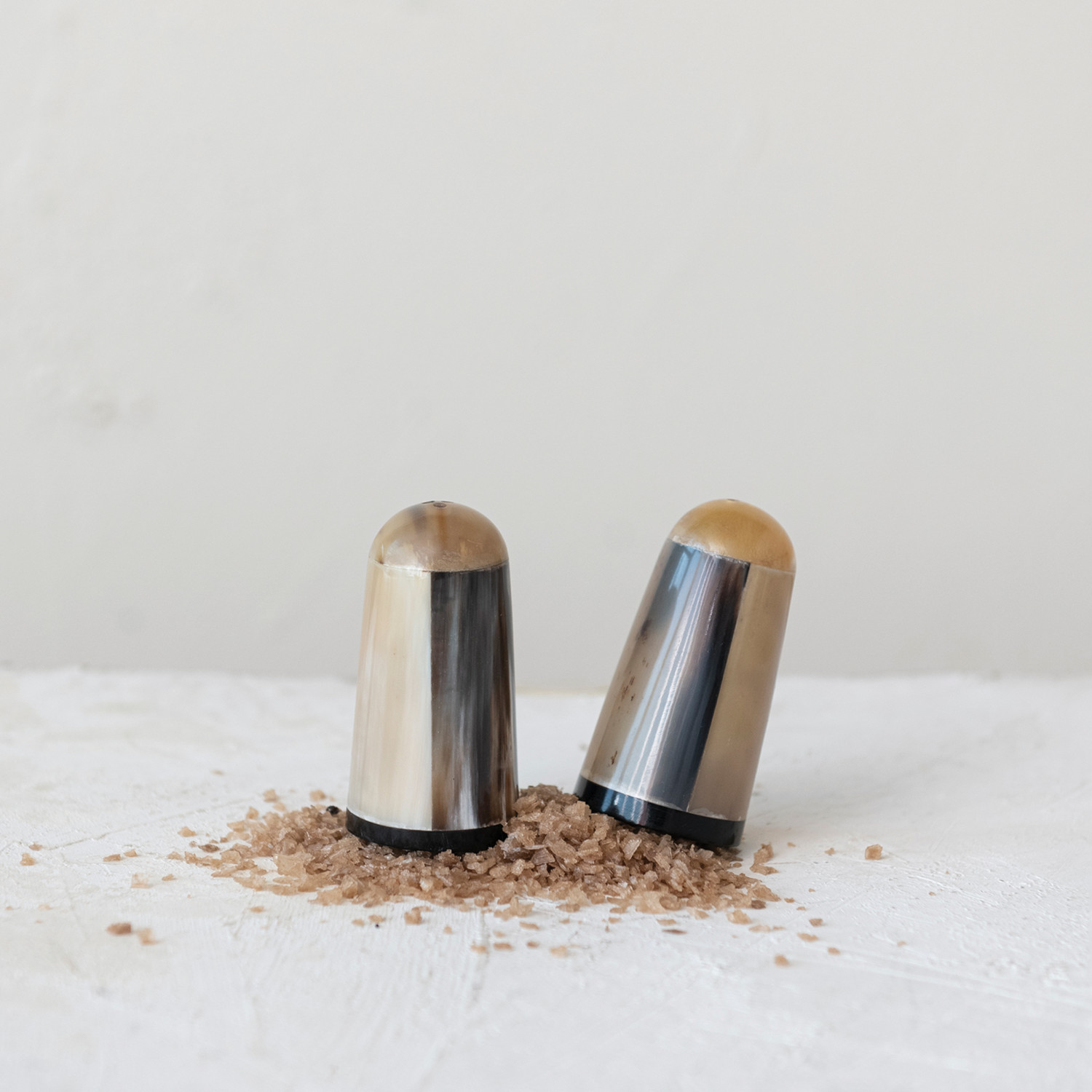 Two natural horn salt and pepper shakers sitting on a pile of rock salt on a white surface with a light gray background.