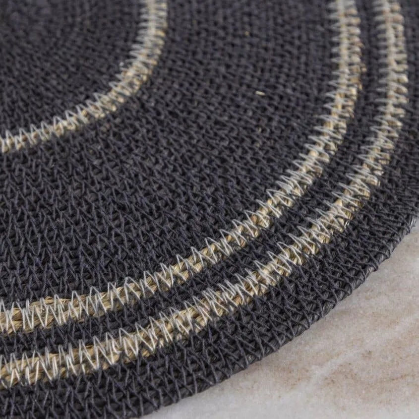 Closeup of a navy blue round woven placemat with contrasting off-white bands on a stone surface