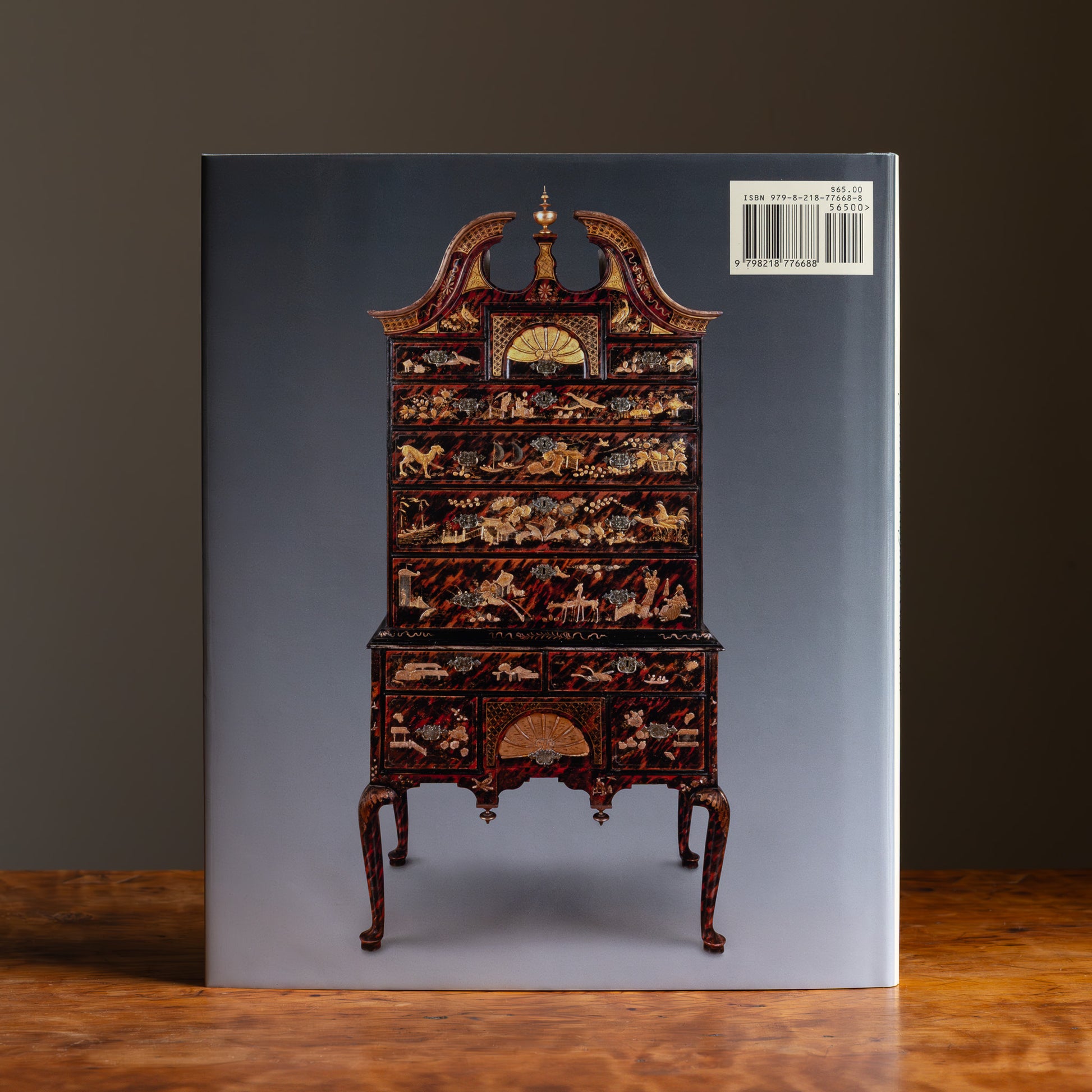 Back cover of book featuring an image of a decorative high chest with intricate gilded accents on a gray background