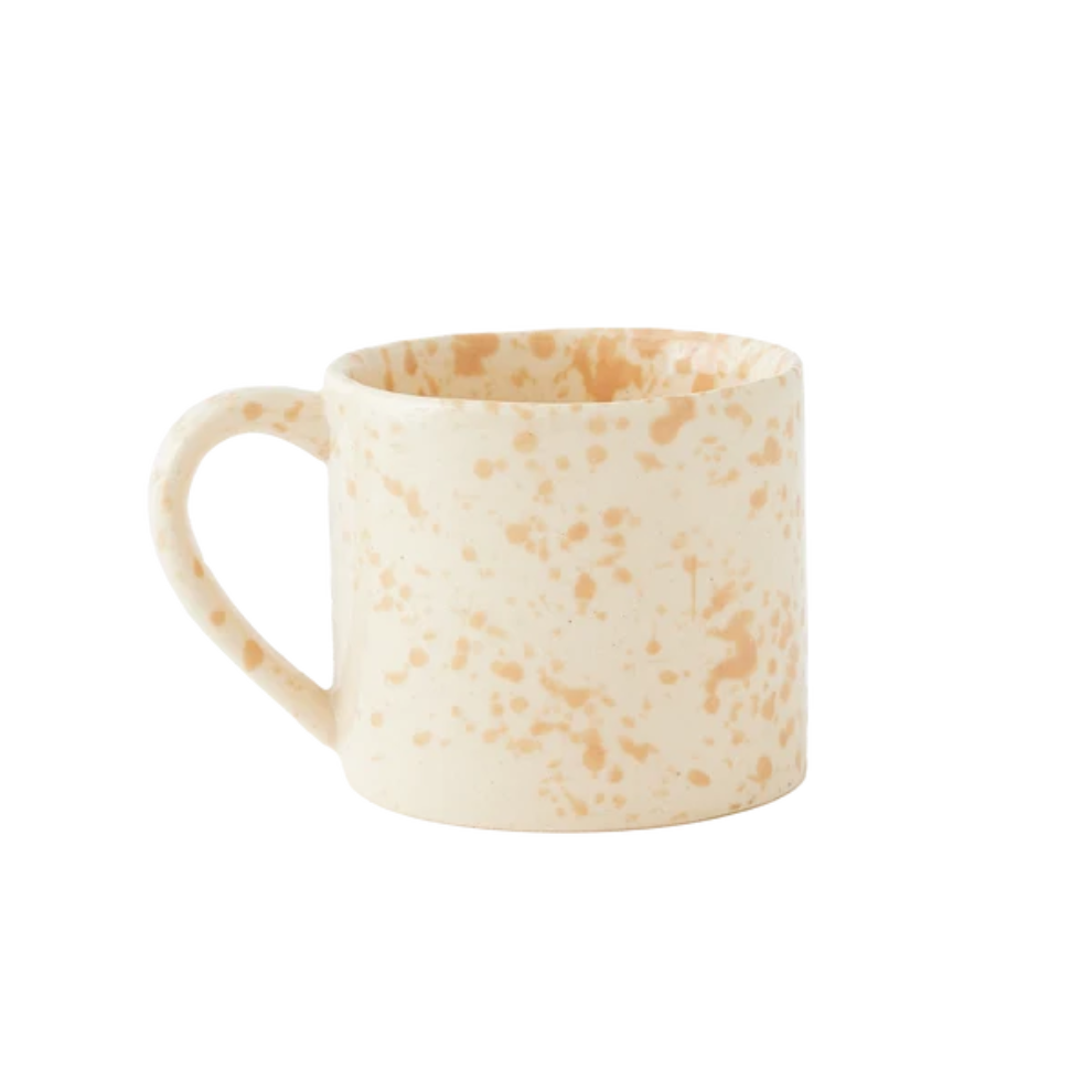 A straight-sided round mug with a warm cream base and translucent light beige splattered pattern, shown against a plain white background.