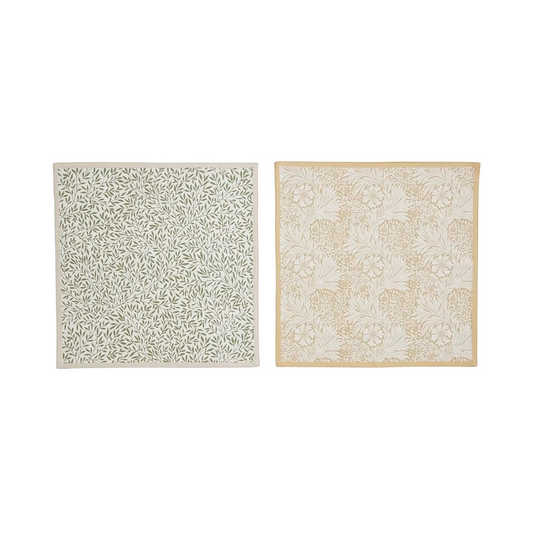 A pair of square cloth napkins displayed side-by-side against a white background. Left napkin features a dense, repeating botanical pattern of small green leaves and vines on a light off-white background with a light beige outer border. Right napkin features a more intricate, larger-scale floral and foliage pattern in muted yellow tone, finished with a solid muted yellow border.