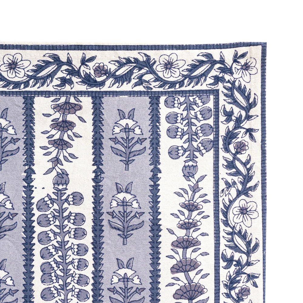 Close-up of the corner of a placemat with a blue and white floral block printed pattern, featuring vertical bands of botanical motifs and a decorative border, shown flat against a white background.