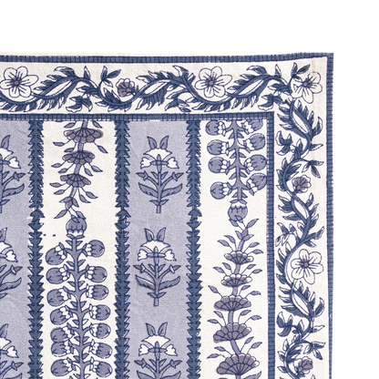 Close-up of the corner of a placemat with a blue and white floral block printed pattern, featuring vertical bands of botanical motifs and a decorative border, shown flat against a white background.