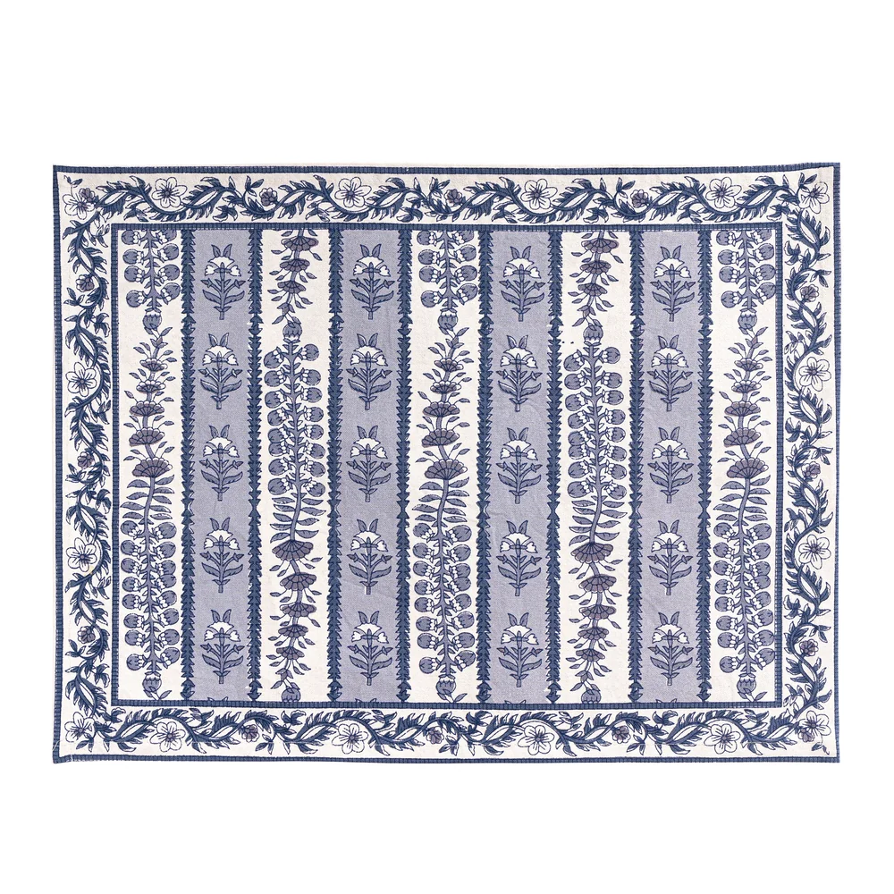 A rectangular placemat with a blue and white floral block printed pattern, featuring vertical bands of botanical motifs and a decorative border, shown flat against a white background.