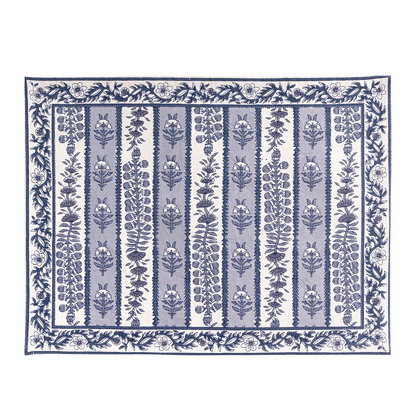 A rectangular placemat with a blue and white floral block printed pattern, featuring vertical bands of botanical motifs and a decorative border, shown flat against a white background.