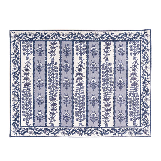 A rectangular placemat with a blue and white floral block printed pattern, featuring vertical bands of botanical motifs and a decorative border, shown flat against a white background.