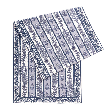 Folded table runner featuring a alternating bands of light blue and white with blue floral block printed designs against a white background.