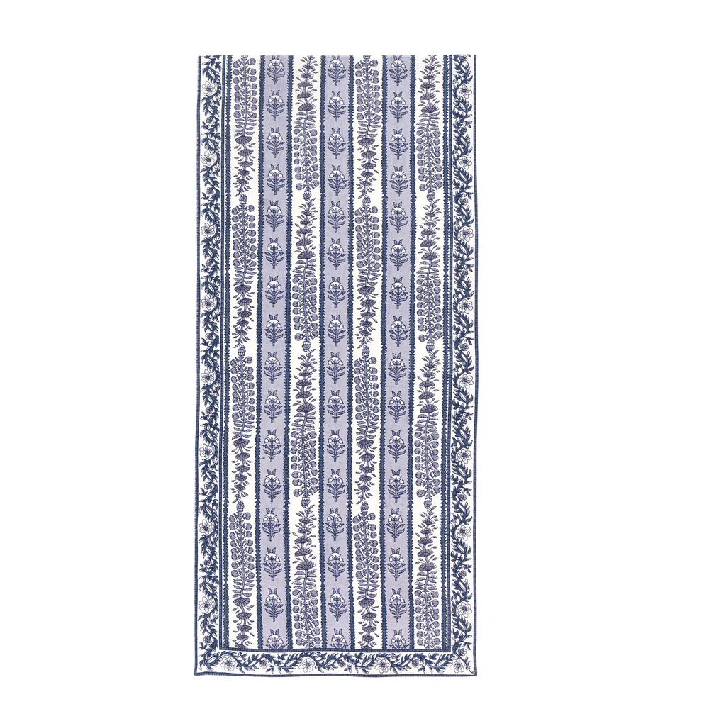 A table runner featuring a alternating bands of light blue and white with blue floral block printed designs against a white background.