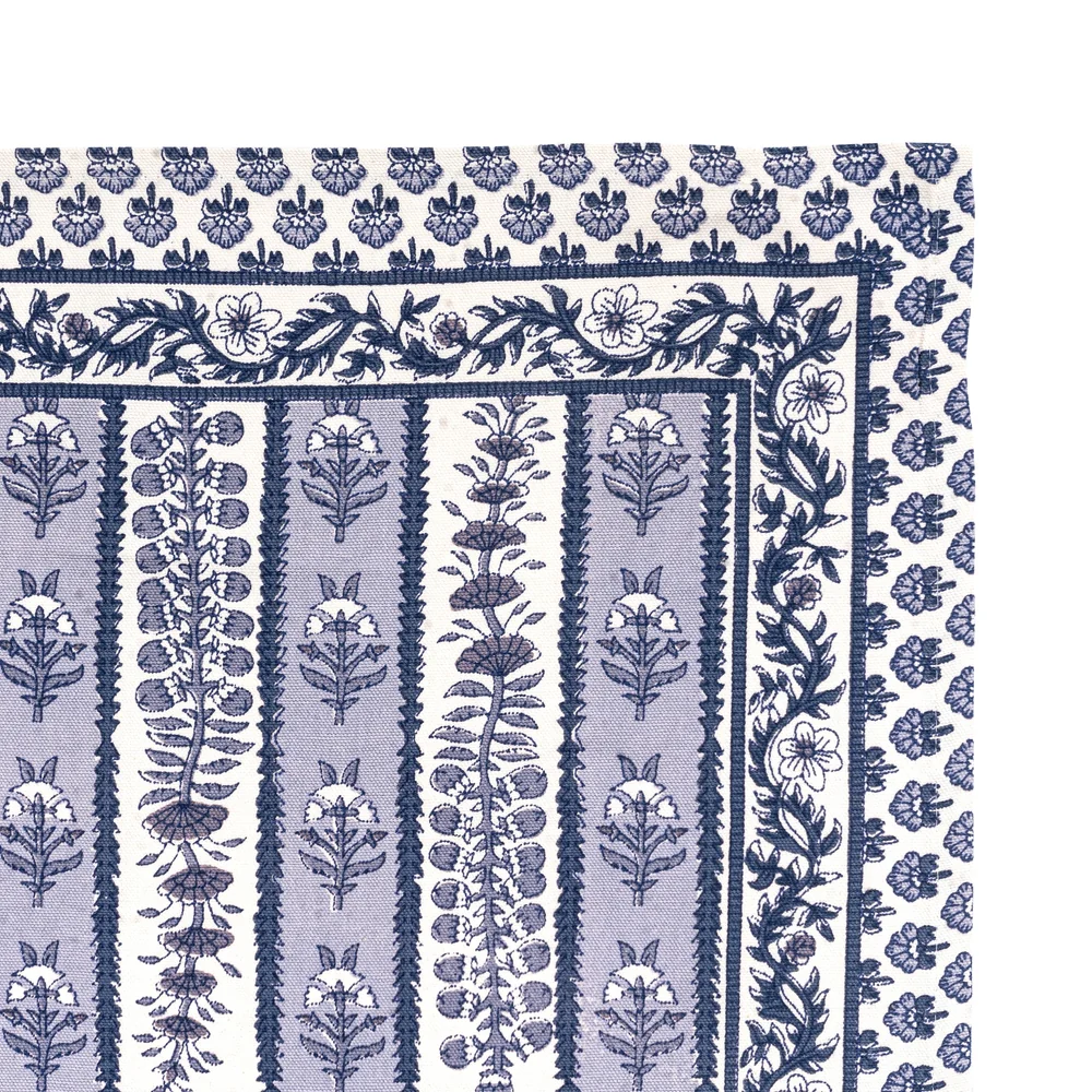 A close-up of the corner of a cotton tea towel featuring a navy blue and light blue floral block print pattern on off-white.