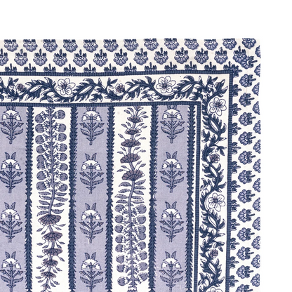 A close-up of the corner of a cotton tea towel featuring a navy blue and light blue floral block print pattern on off-white.
