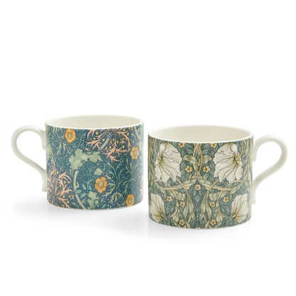 Two William Morris floral-patterned mugs in shades of blues, greens and yellows side-by-side on a white background
