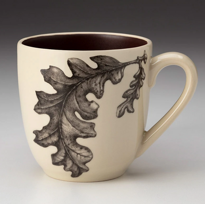 An off-white stoneware tapered mug featuring a sketch of oak leaves in black and a dark brown interior.