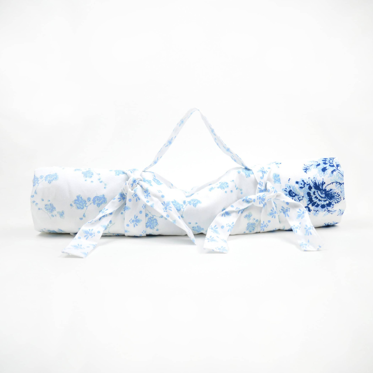 White and blue floral travel picnic blanket rolled up and tied with attached matching straps and carrying handle against a white background