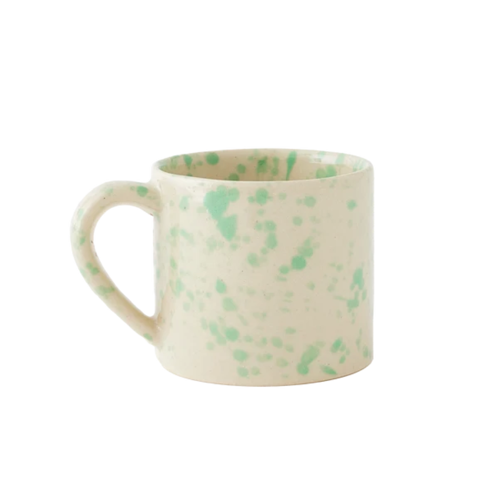 A straight-sided round mug with a warm cream base and translucent light seafoam-green splattered pattern, shown against a plain white background.