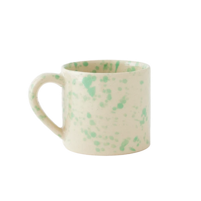 A straight-sided round mug with a warm cream base and translucent light seafoam-green splattered pattern, shown against a plain white background.