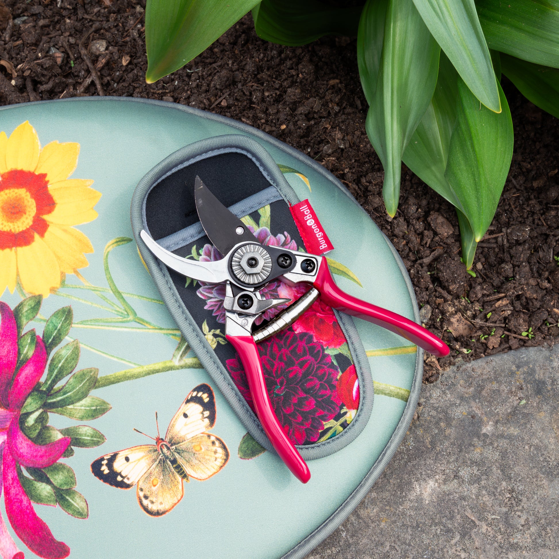 Gardening shears on a floral-patterned kneeler with plants in the background