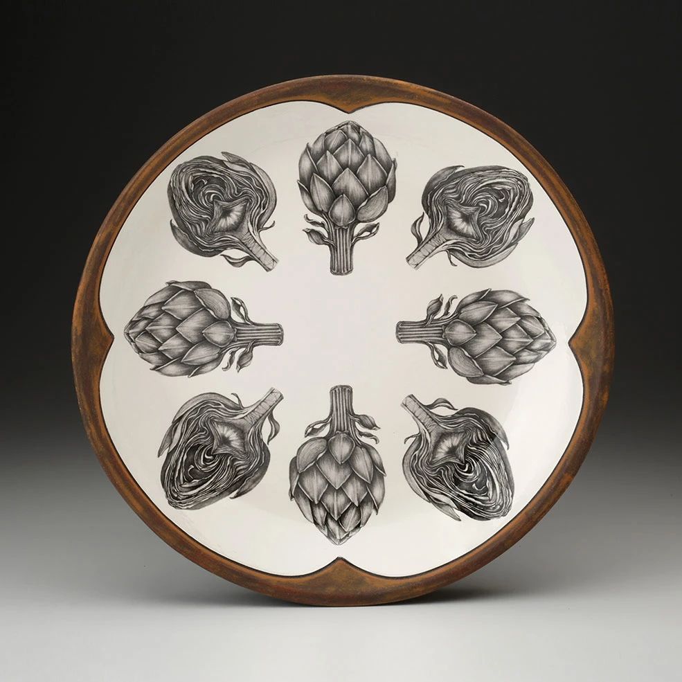 An off-white round serving platter with a rust-brown rim featuring a sketches of artichokes in black arranged in a circle.