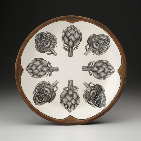 An off-white round serving platter with a rust-brown rim featuring a sketches of artichokes in black arranged in a circle.