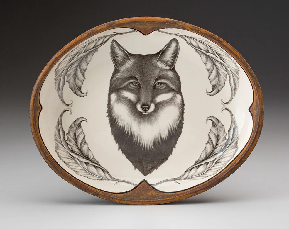 An off-white oval serving plate with a rust-brown rim featuring a sketch of a fox portrait framed with leaves in black 