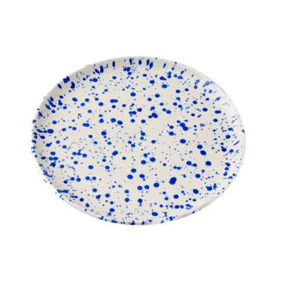 Round ceramic plate with a cream-colored base decorated with a translucent cobalt blue splattered pattern on a white background