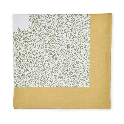 Corner detail of a folded cotton tablecloth featuring a green leaf pattern on off-white and a yellow border.
